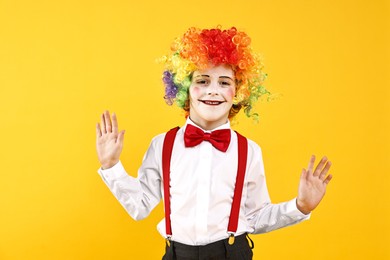 Photo of Happy little boy dressed like clown on yellow background. Surprise party