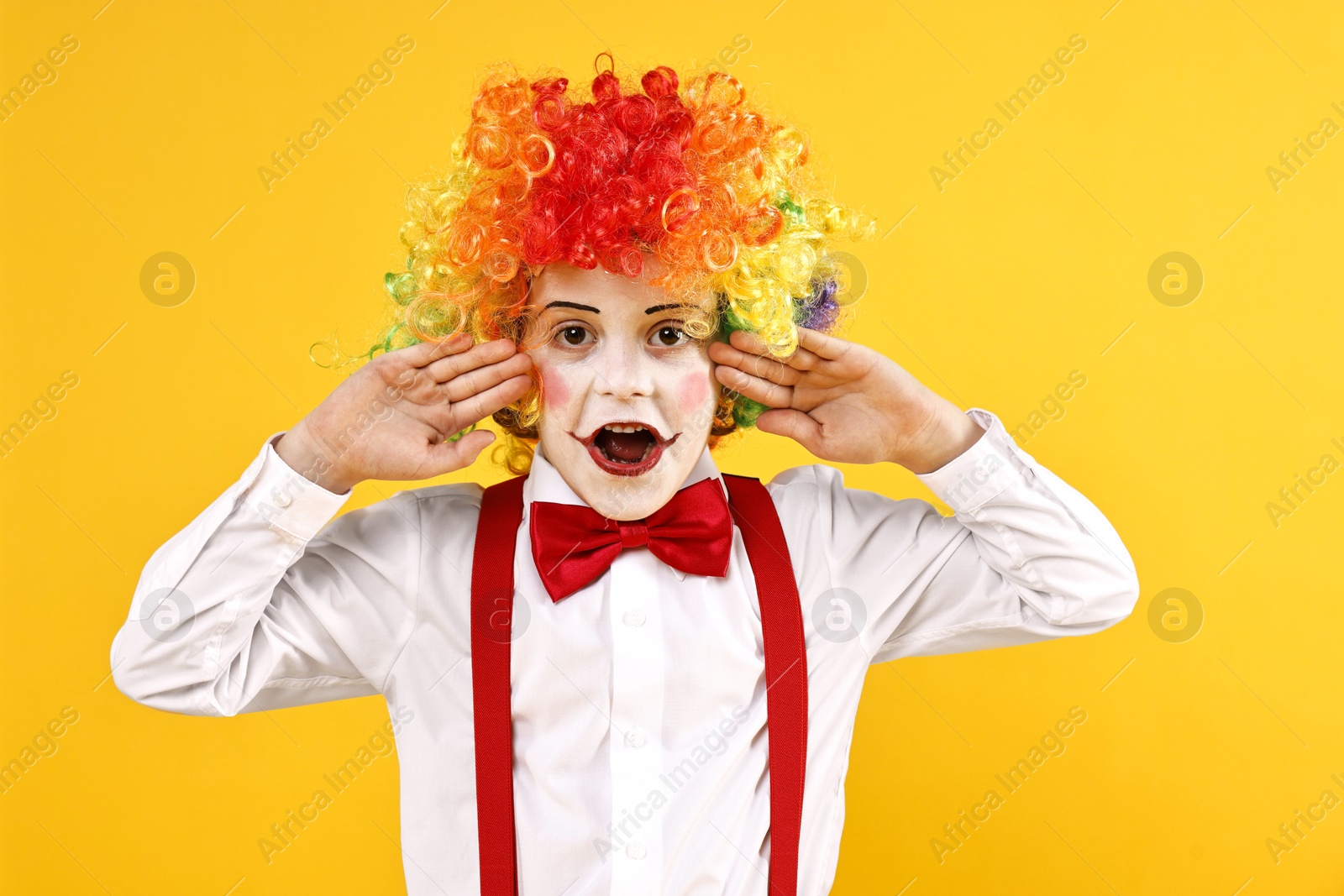 Photo of Emotional little boy dressed like clown on yellow background. Surprise party