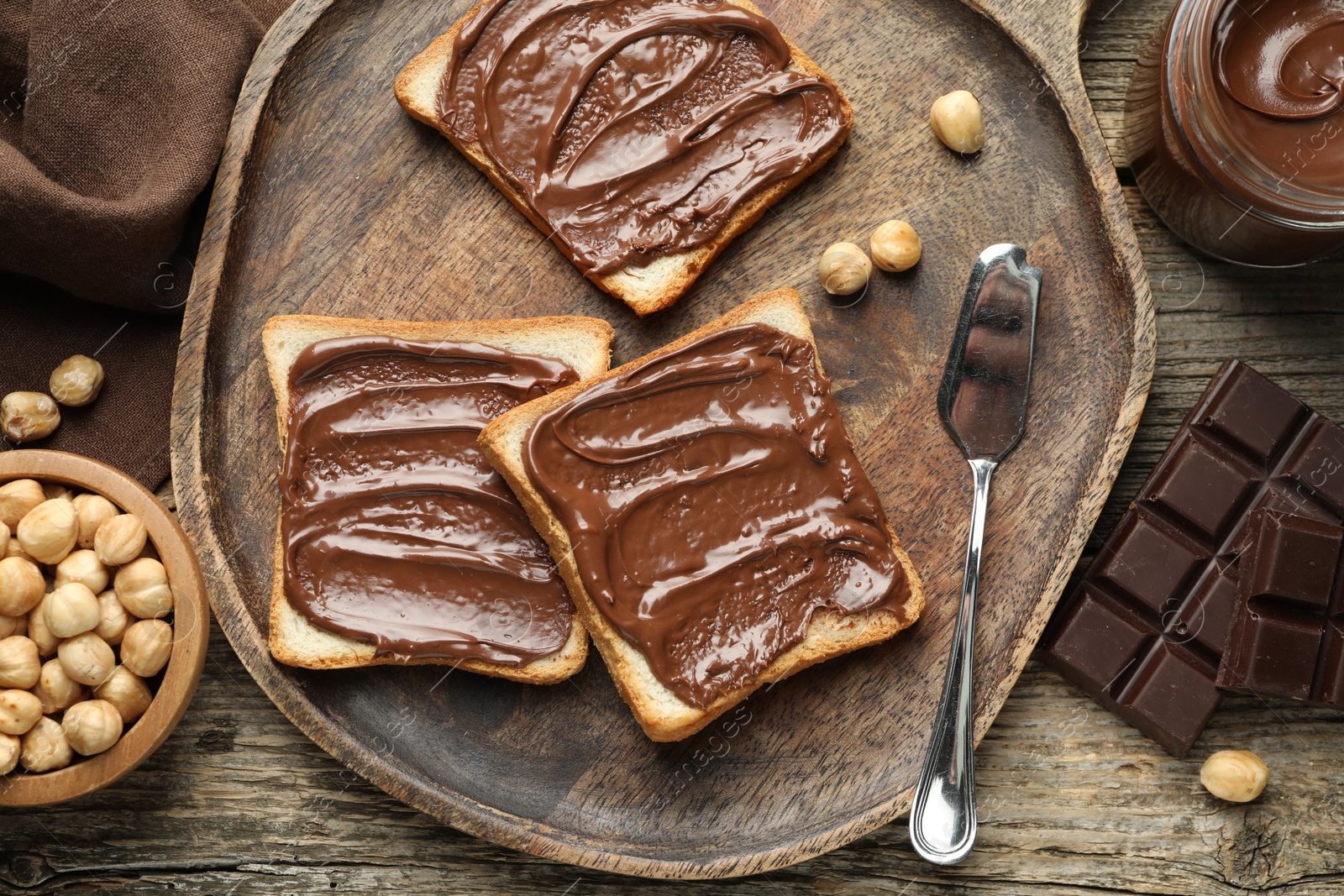 Photo of Tasty sandwiches with chocolate butter and hazelnuts on wooden table, flat lay