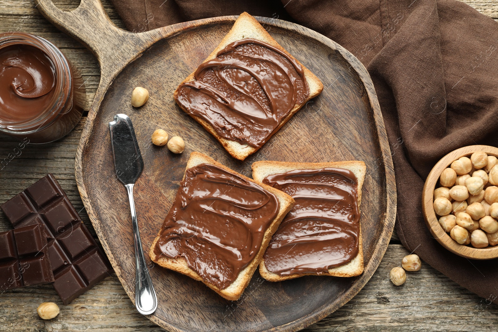 Photo of Tasty sandwiches with chocolate butter and hazelnuts on wooden table, flat lay