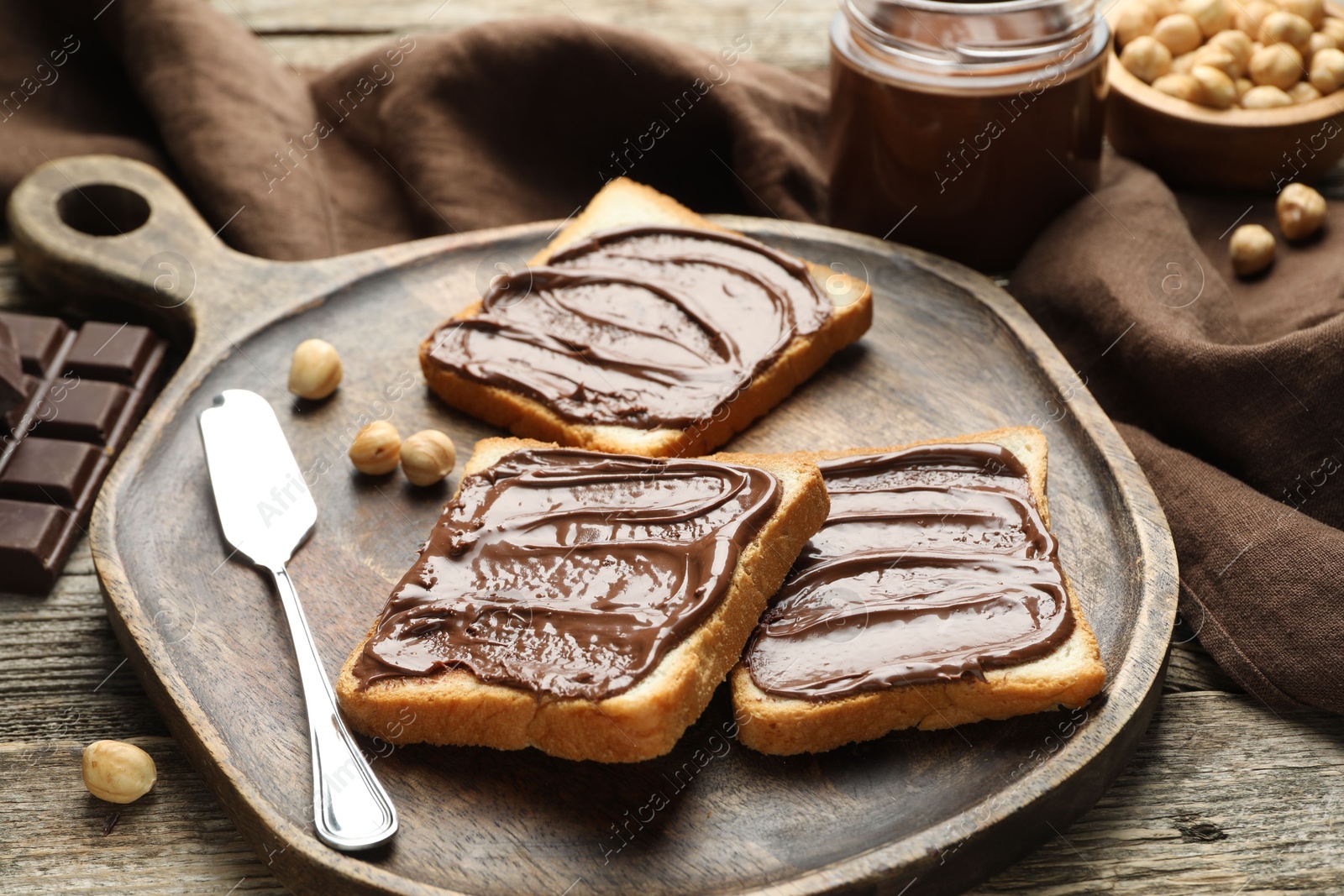 Photo of Tasty sandwiches with chocolate butter and hazelnuts on wooden table, closeup