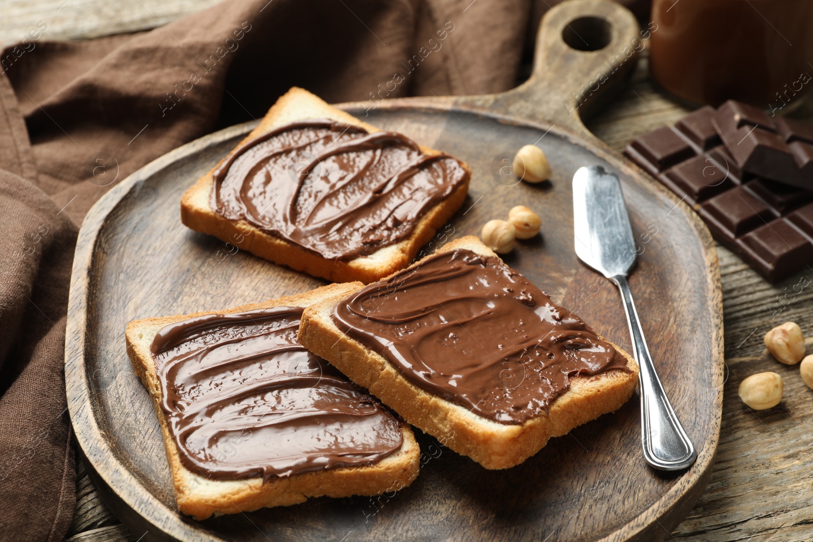 Photo of Tasty sandwiches with chocolate butter and hazelnuts on wooden table, closeup