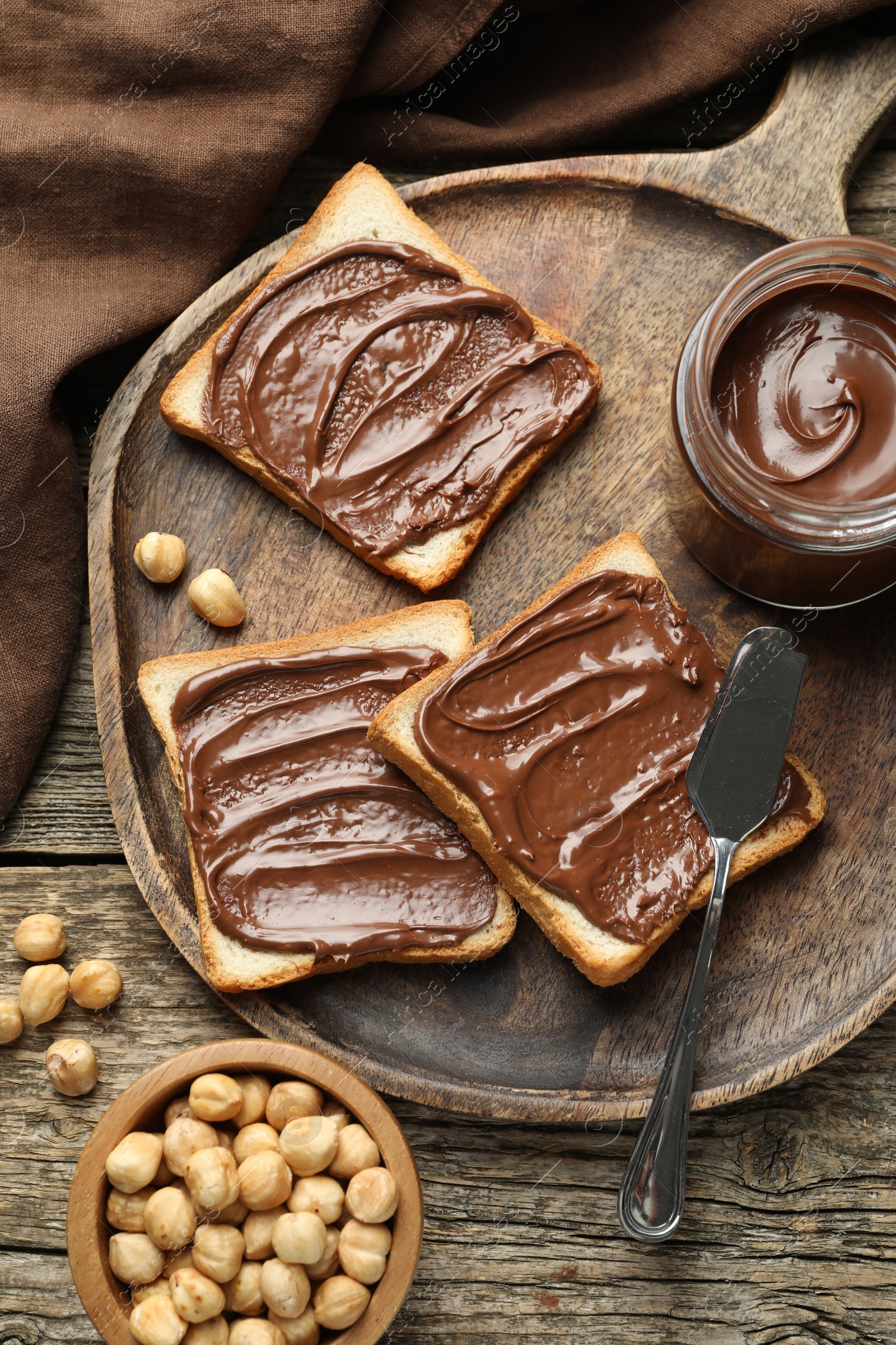 Photo of Tasty sandwiches with chocolate butter and hazelnuts on wooden table, flat lay