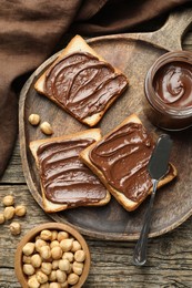 Photo of Tasty sandwiches with chocolate butter and hazelnuts on wooden table, flat lay