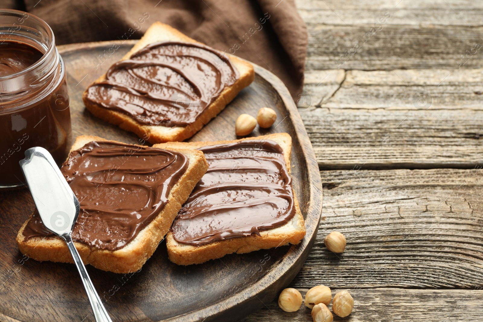 Photo of Tasty sandwiches with chocolate butter and hazelnuts on wooden table, closeup. Space for text