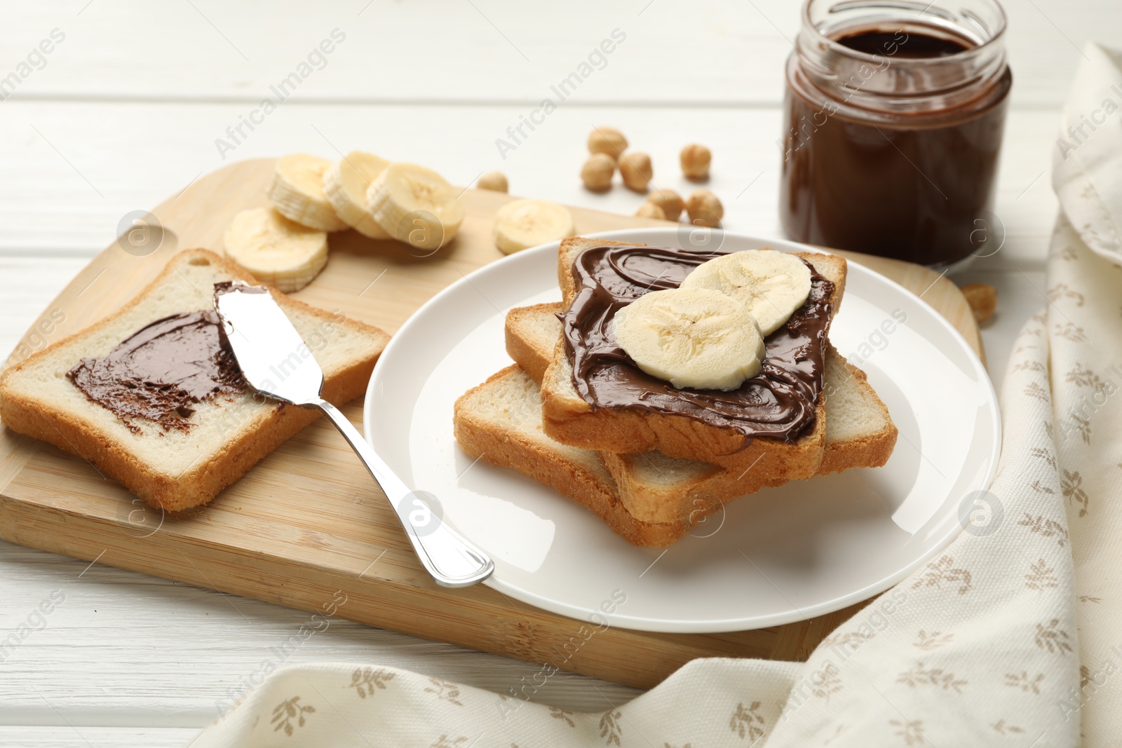 Photo of Sandwiches with chocolate butter, bananas and hazelnuts on white wooden table, closeup