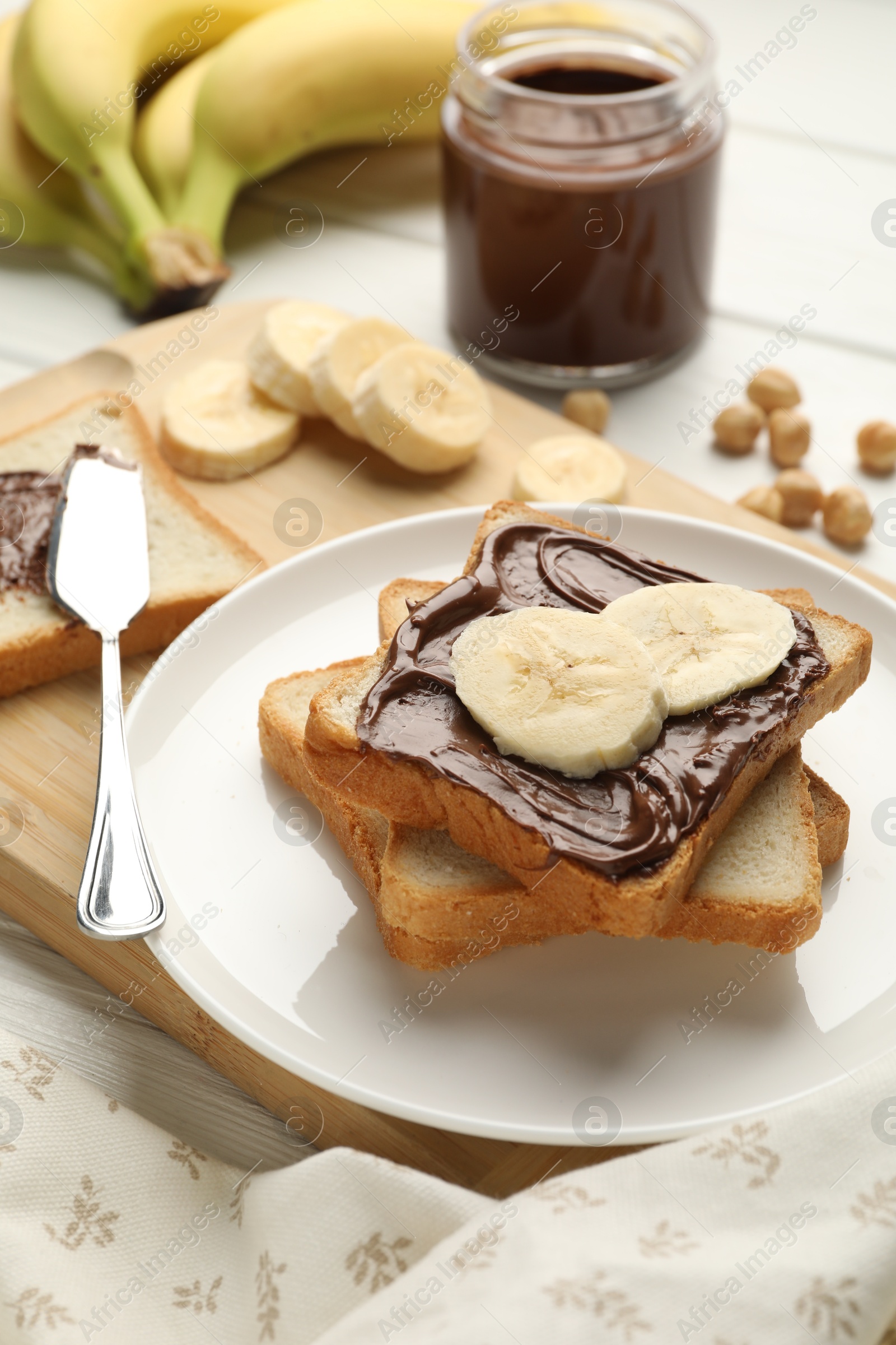 Photo of Sandwiches with chocolate butter, bananas and hazelnuts on white wooden table, closeup