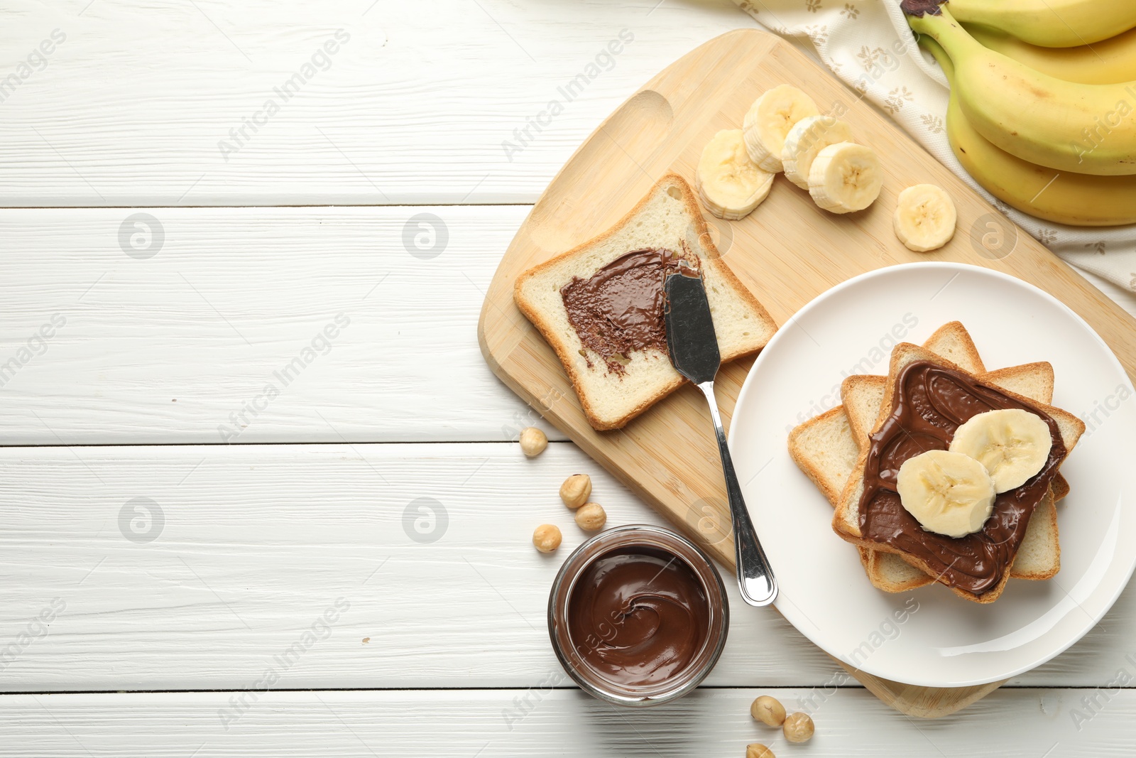 Photo of Sandwiches with chocolate butter, bananas and hazelnuts on white wooden table, flat lay. Space for text