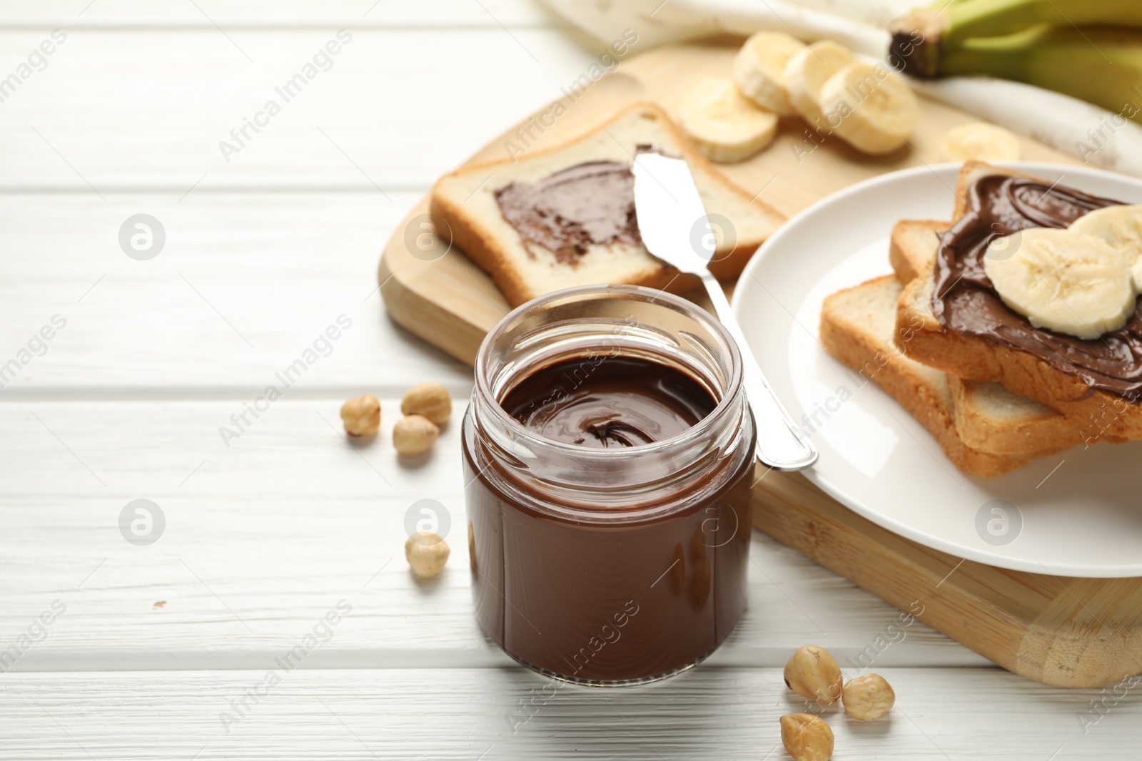 Photo of Sandwiches with chocolate butter, bananas and hazelnuts on white wooden table, closeup. Space for text