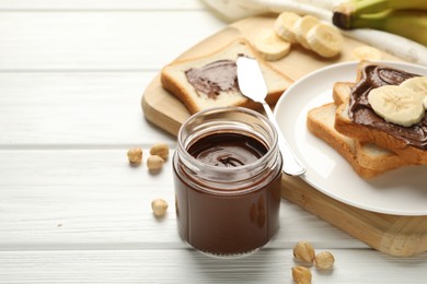 Sandwiches with chocolate butter, bananas and hazelnuts on white wooden table, closeup. Space for text