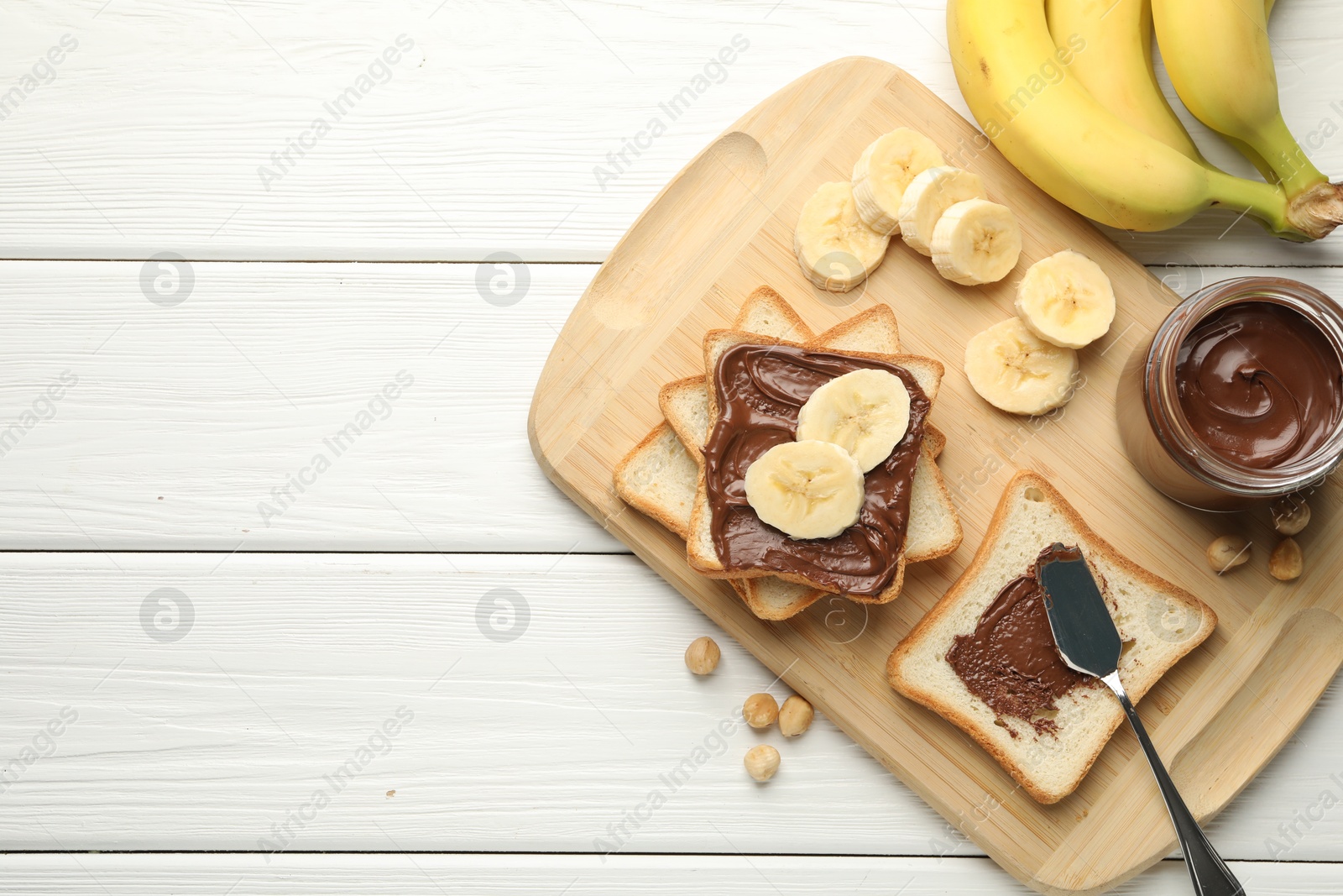 Photo of Sandwiches with chocolate butter, bananas and hazelnuts on white wooden table, flat lay. Space for text