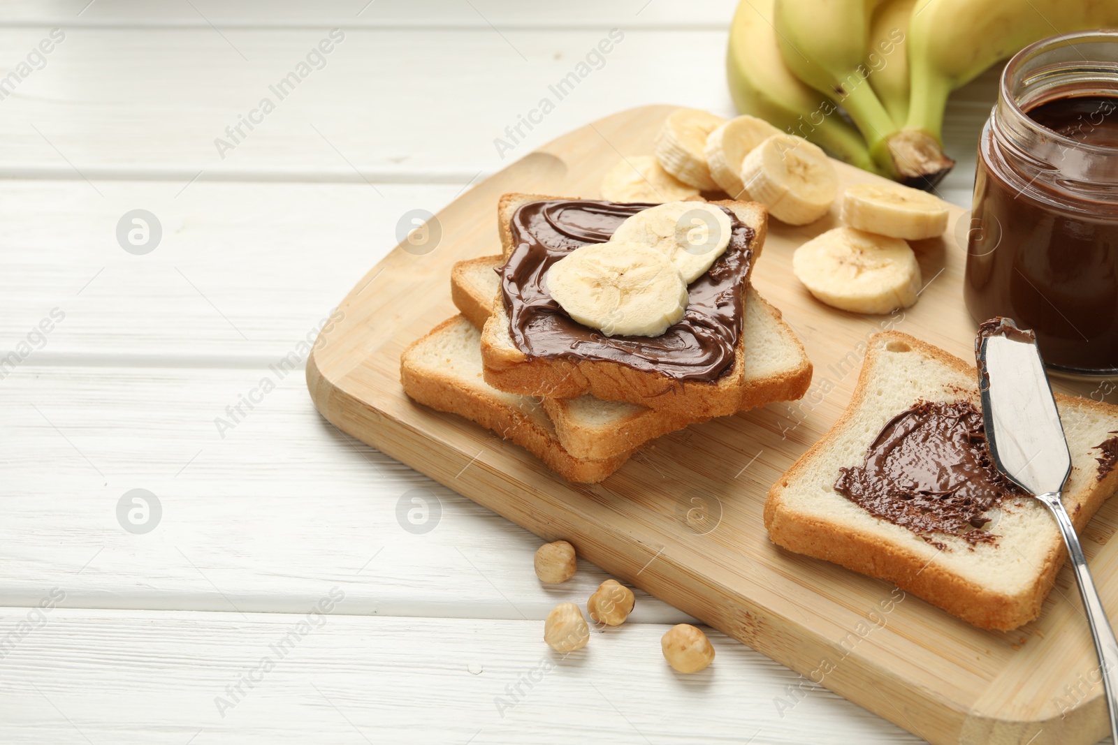 Photo of Sandwiches with chocolate butter, bananas and hazelnuts on white wooden table, closeup. Space for text