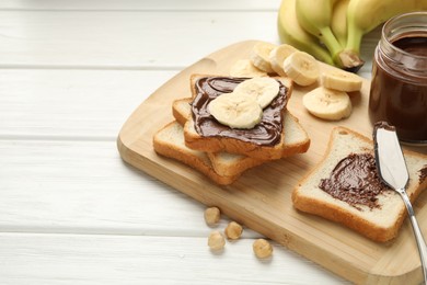 Photo of Sandwiches with chocolate butter, bananas and hazelnuts on white wooden table, closeup. Space for text