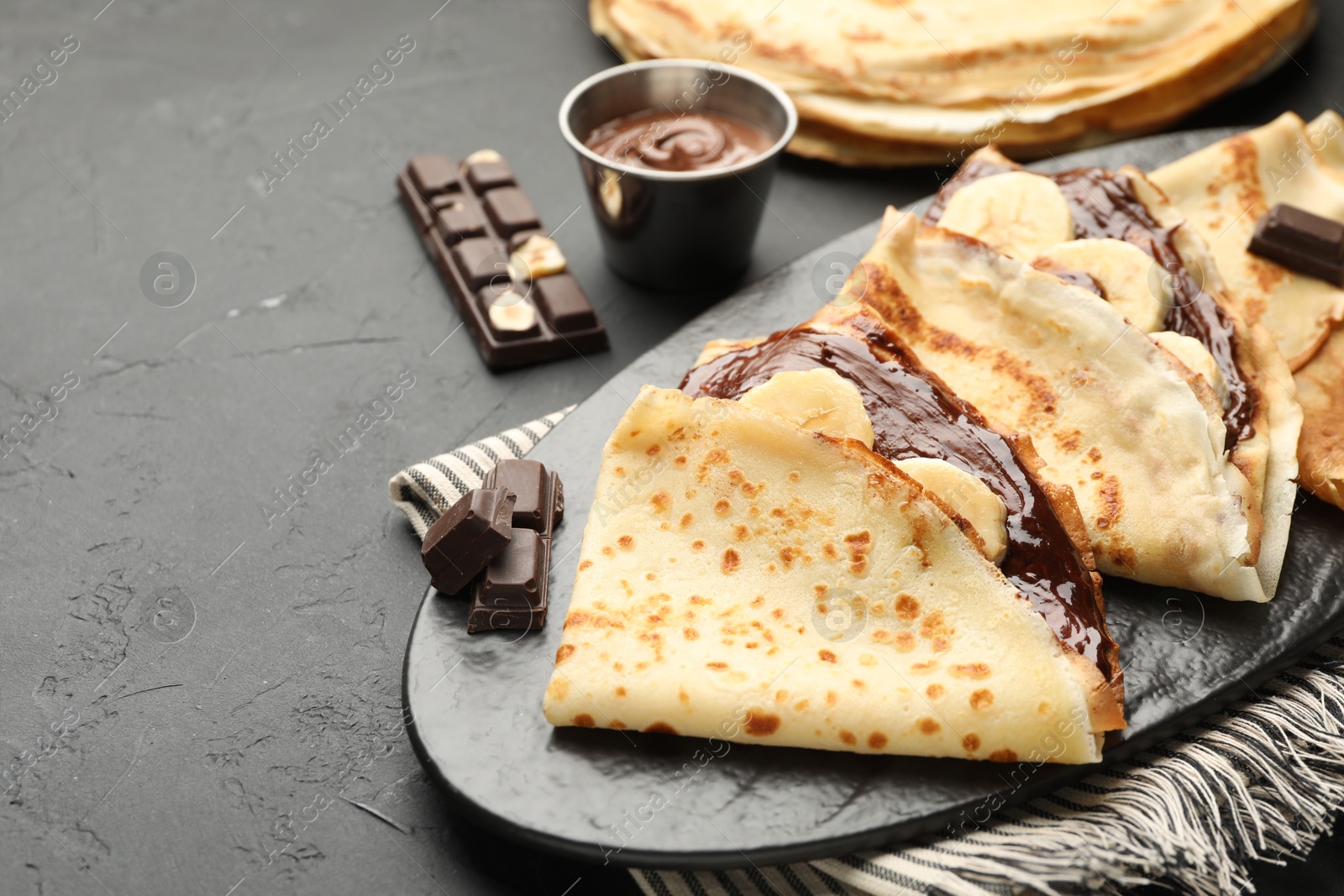 Photo of Tasty crepes with chocolate butter and banana on black table, closeup. Space for text