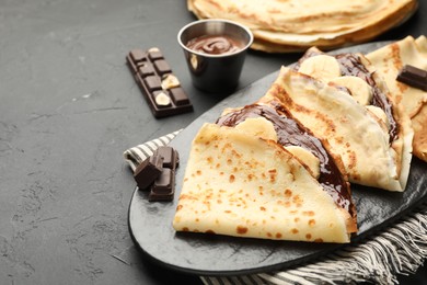 Photo of Tasty crepes with chocolate butter and banana on black table, closeup. Space for text