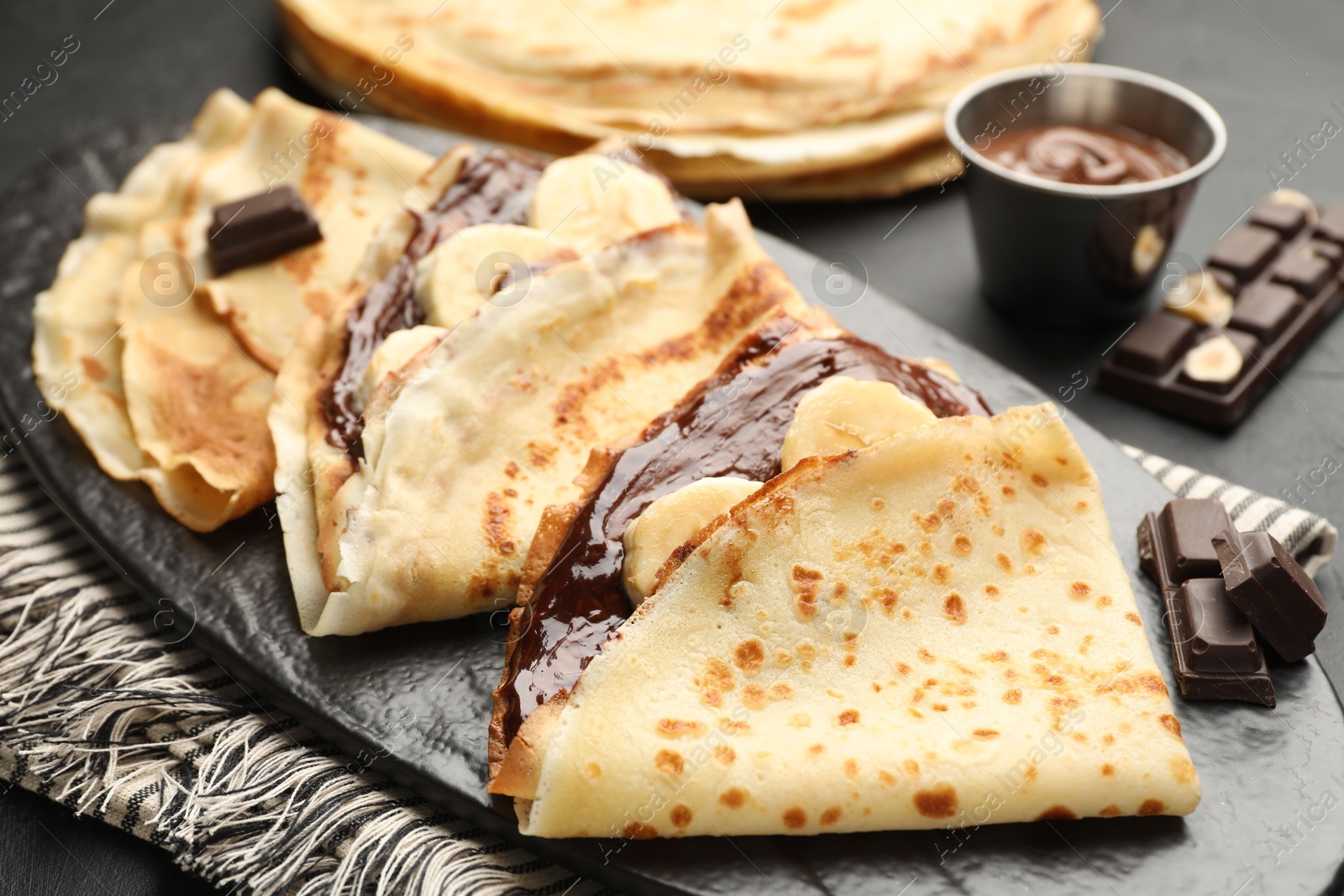 Photo of Tasty crepes with chocolate butter and banana on black table, closeup