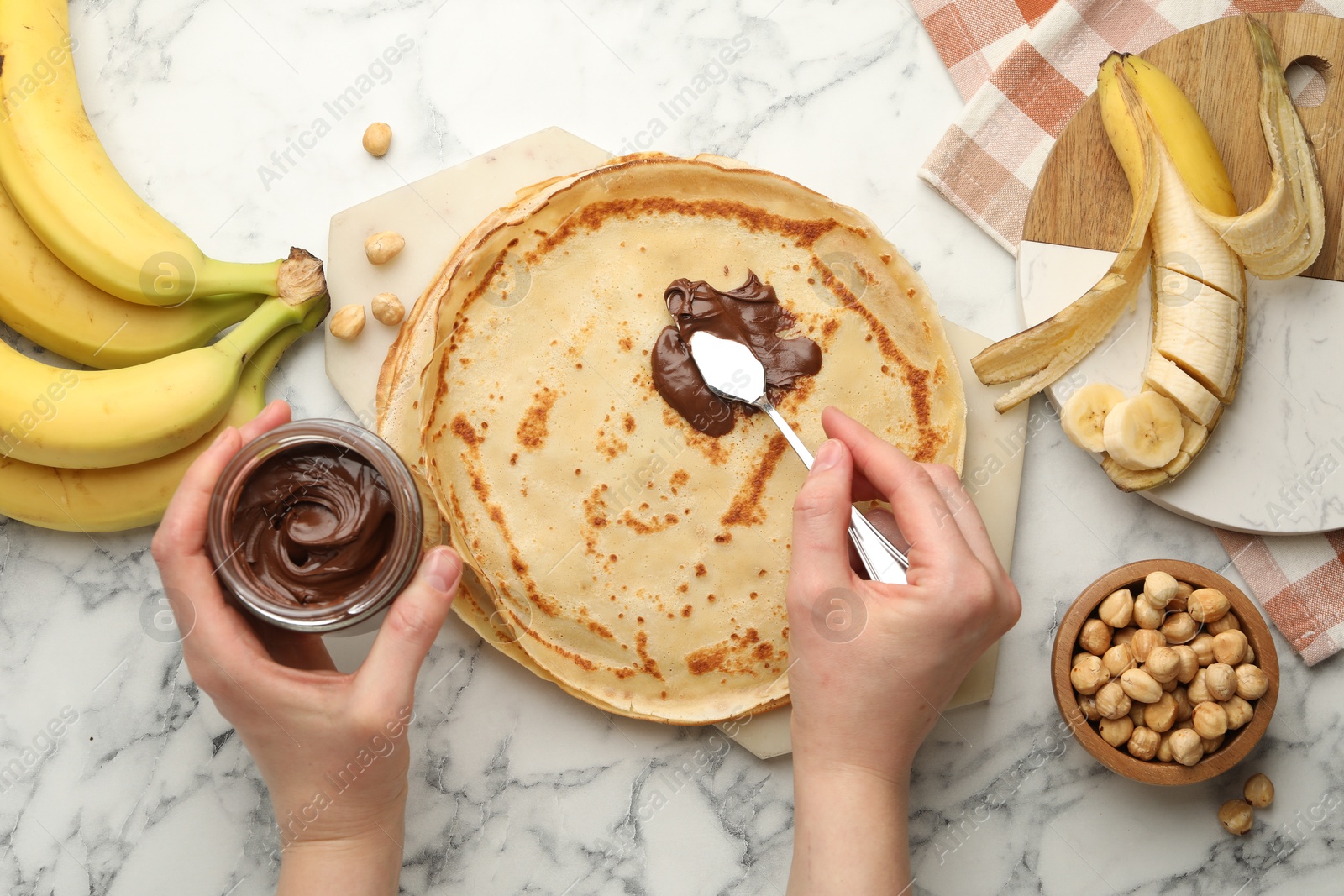 Photo of Woman spreading tasty chocolate butter onto crepe at white marble table, top view