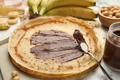 Photo of Tasty crepes with chocolate butter, bananas and hazelnuts on table, closeup