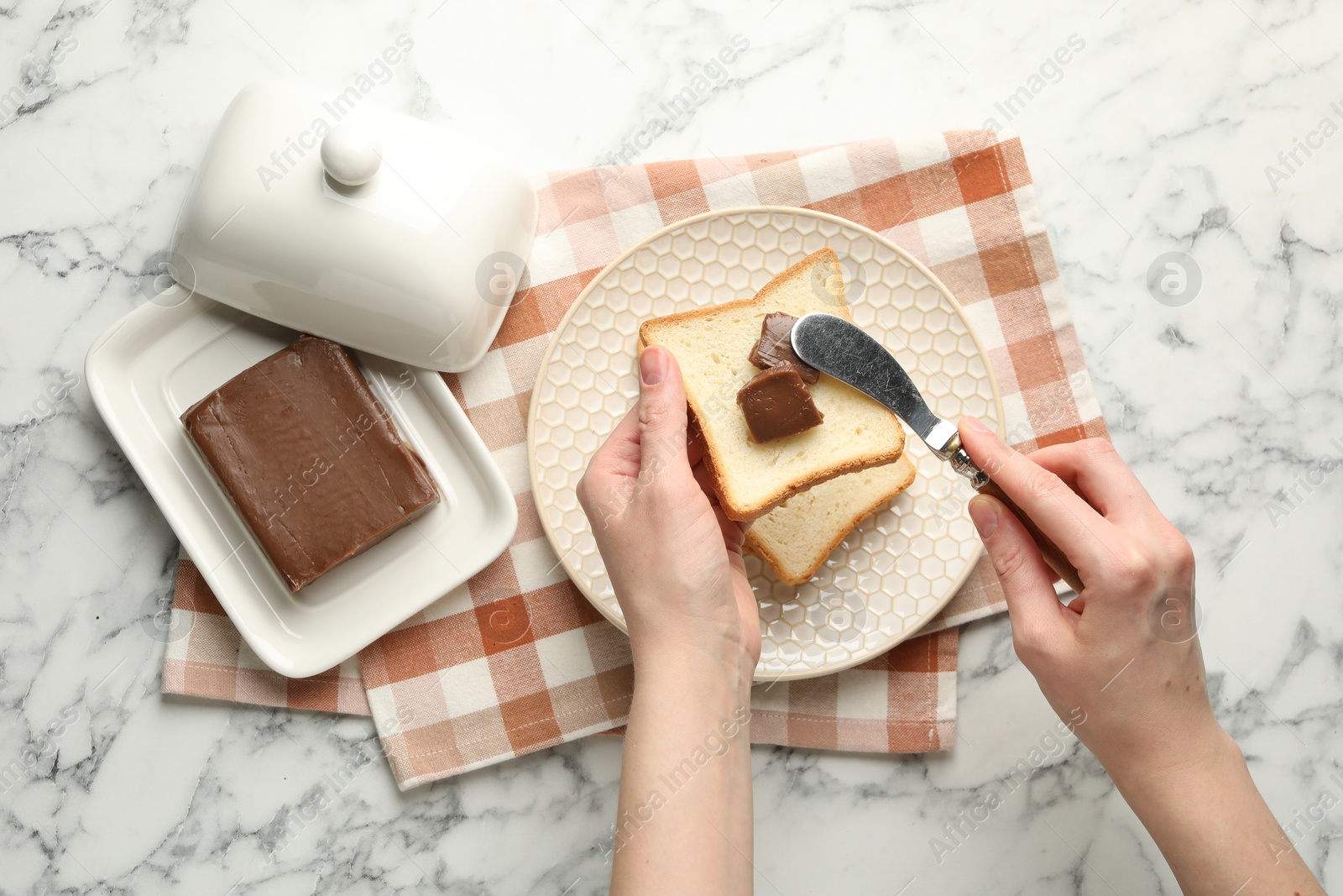 Photo of Woman spreading tasty chocolate butter onto bread at white marble table, top view