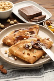 Photo of Tasty crepes with chocolate butter, nuts, honey and knife on table, closeup