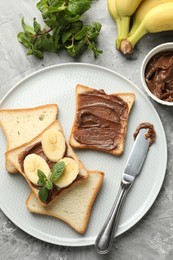 Photo of Sandwiches with chocolate butter, bananas, mint and knife on grey table, flat lay