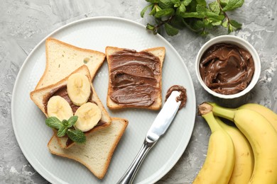 Photo of Sandwiches with chocolate butter, bananas, mint and knife on grey table, flat lay