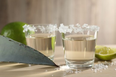 Photo of Tequila shots with salt, lime slice and agave leaf on wooden table, closeup