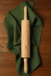 Photo of Rolling pin and green napkin on wooden table, top view