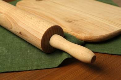 Photo of Rolling pin and green napkin on wooden table, closeup