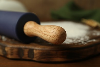 Photo of Rolling pin, wooden board and flour on table, closeup