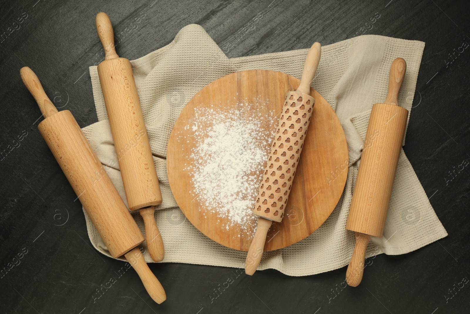 Photo of Wooden rolling pins, board and flour on dark gray textured table, flat lay