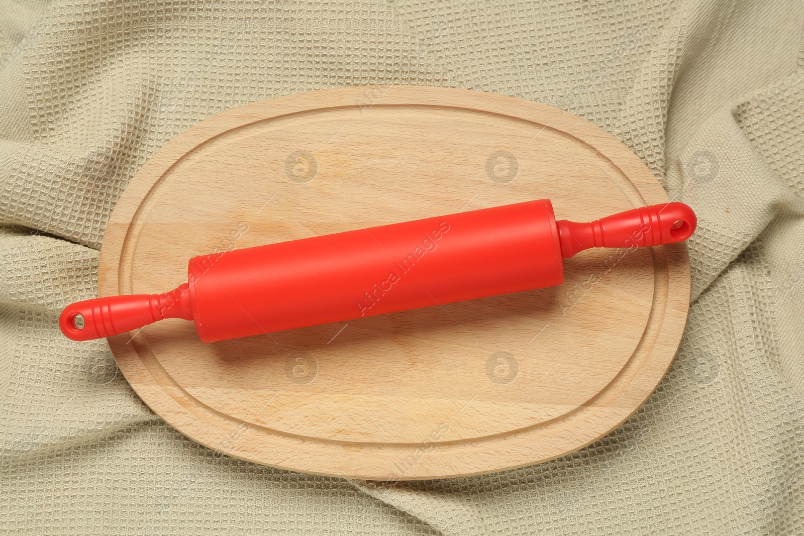 Photo of Red rolling pin and wooden board on beige napkin, top view