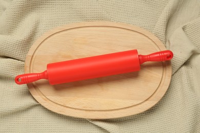 Photo of Red rolling pin and wooden board on beige napkin, top view