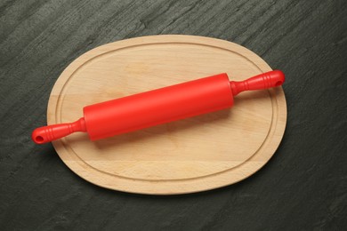 Photo of Red rolling pin and wooden board on dark gray textured table, top view