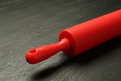 Photo of Red rolling pin on dark gray textured table, closeup