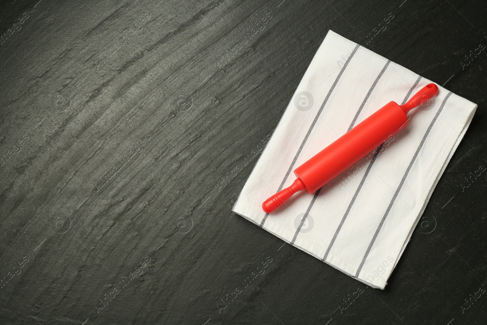 Photo of Red rolling pin and napkin on dark gray textured table, top view. Space for text