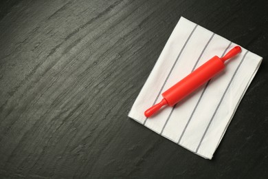 Photo of Red rolling pin and napkin on dark gray textured table, top view. Space for text