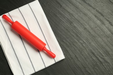 Photo of Red rolling pin and napkin on dark gray textured table, top view. Space for text