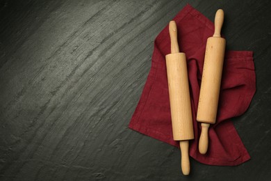 Photo of Wooden rolling pins and napkin on dark gray textured table, flat lay. Space for text