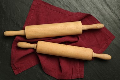 Photo of Wooden rolling pins and napkin on dark gray textured table, flat lay