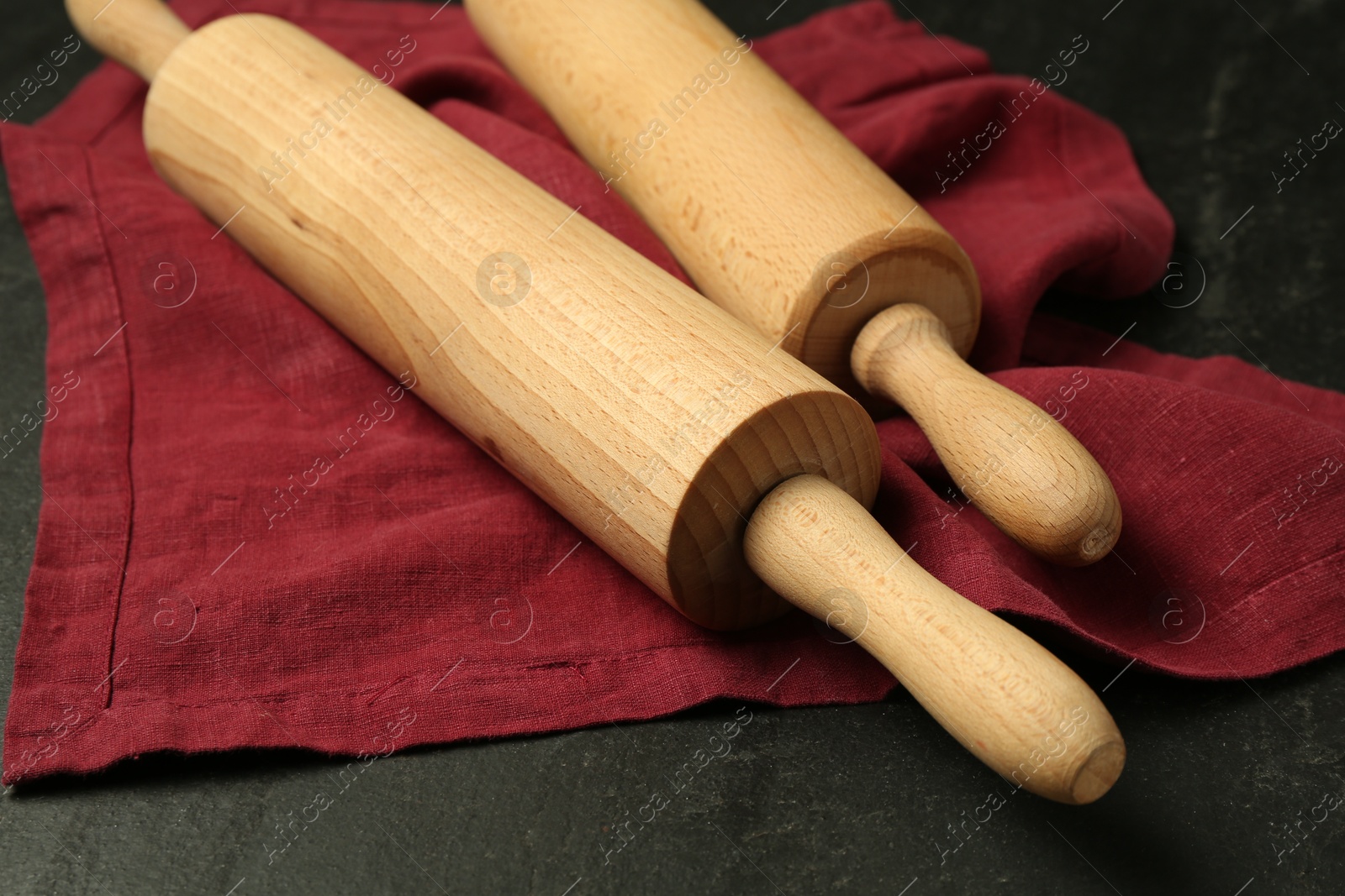 Photo of Wooden rolling pins and napkin on dark gray textured table, closeup