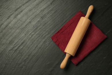 Photo of Wooden rolling pin and napkin on dark gray textured table, top view. Space for text