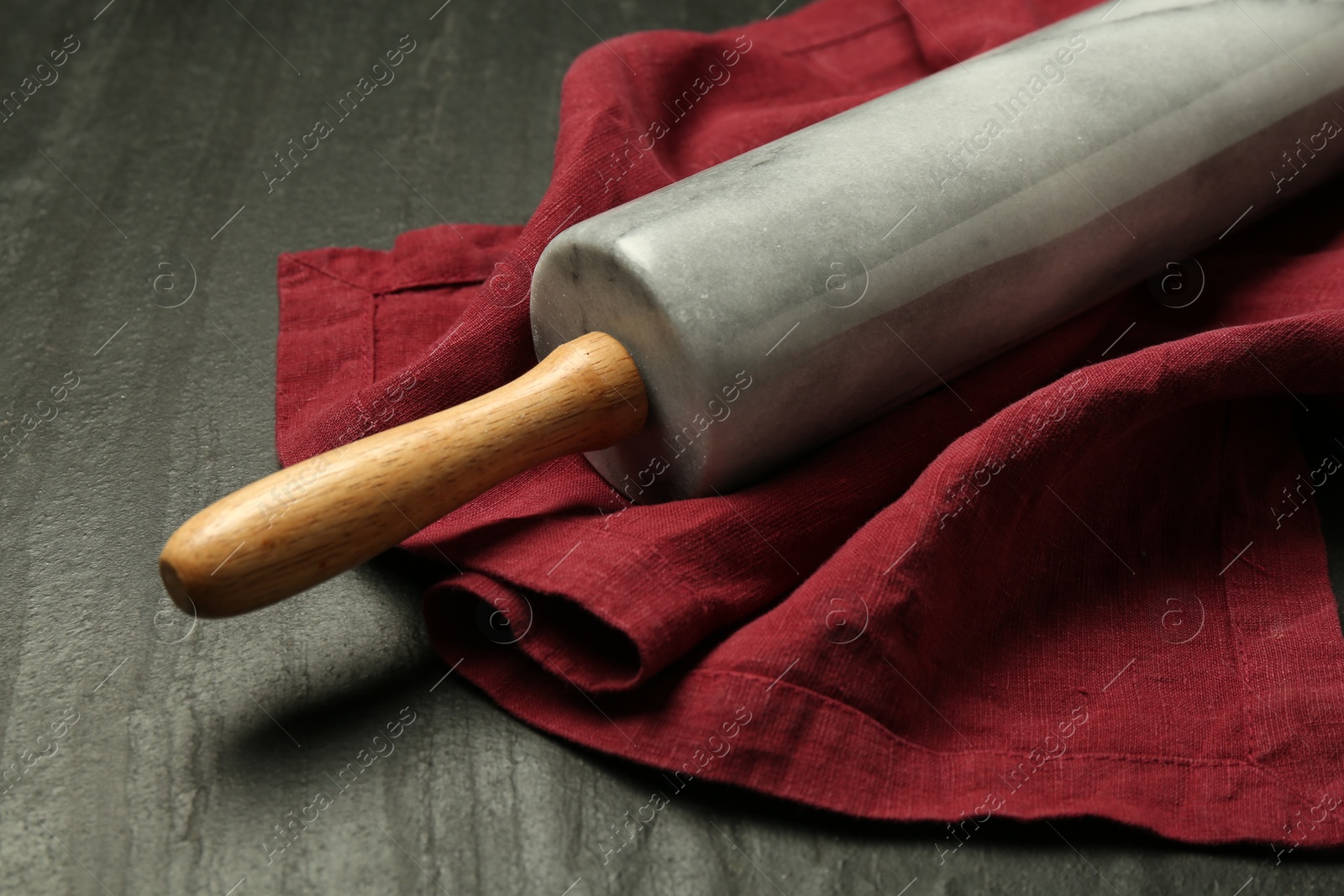 Photo of Rolling pin and napkin on dark gray textured table, closeup