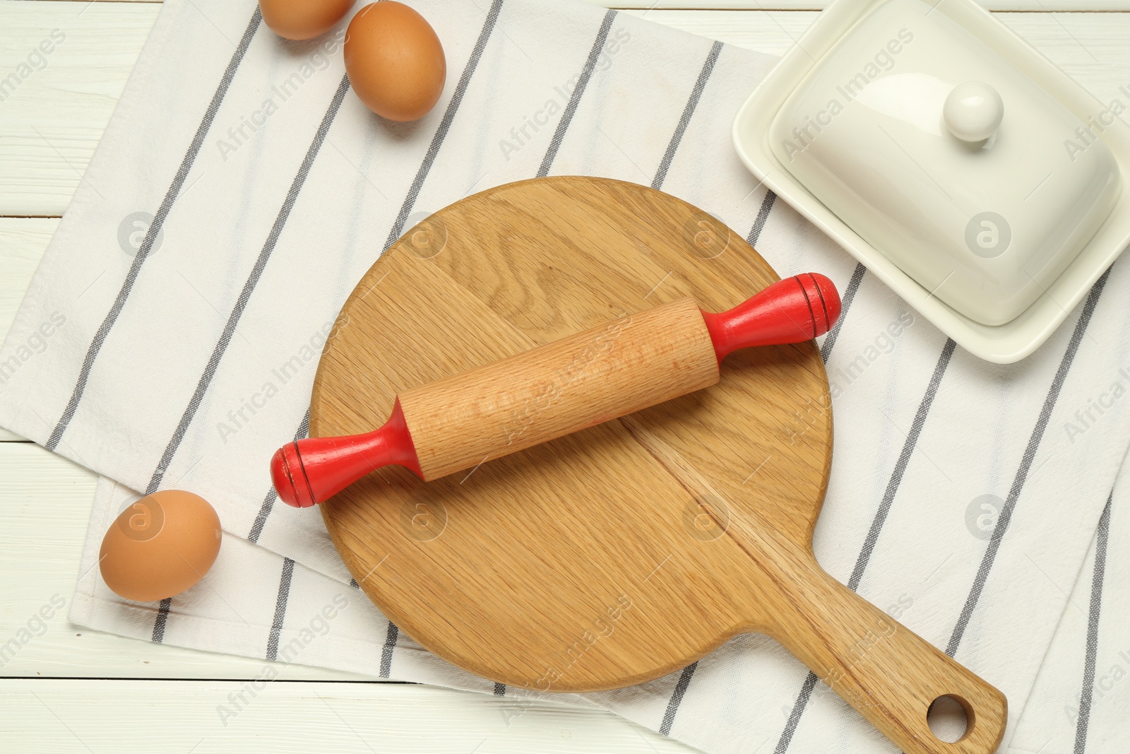 Photo of Rolling pin, board, eggs and butter dish on white table, flat lay