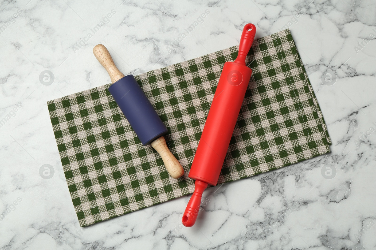 Photo of Rolling pins and checkered napkin on light marble table, flat lay