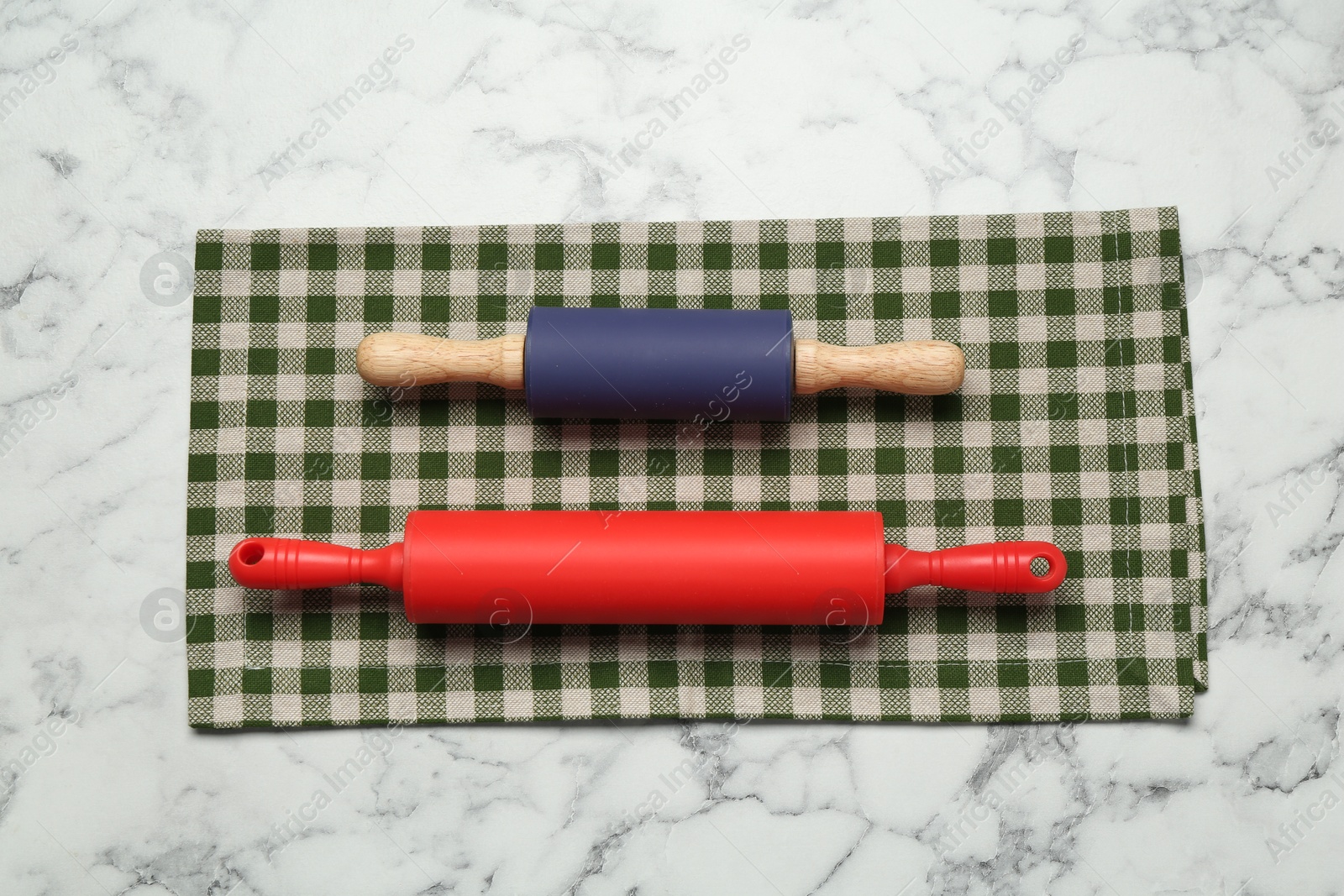 Photo of Rolling pins and checkered napkin on light marble table, flat lay