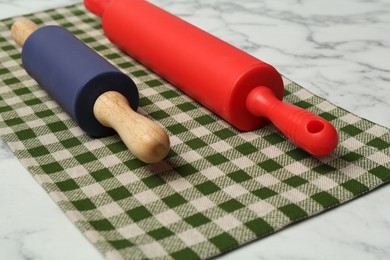 Photo of Rolling pins and checkered napkin on light marble table, closeup