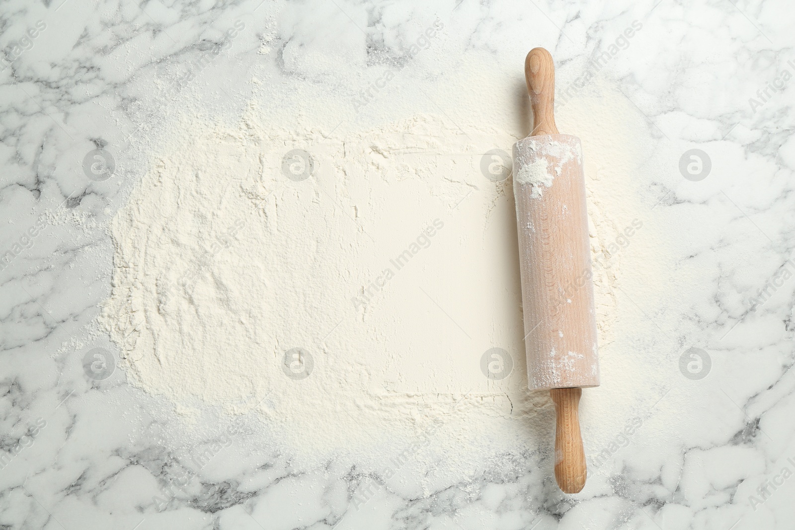 Photo of Rolling pin and flour on light marble table, top view. Space for text