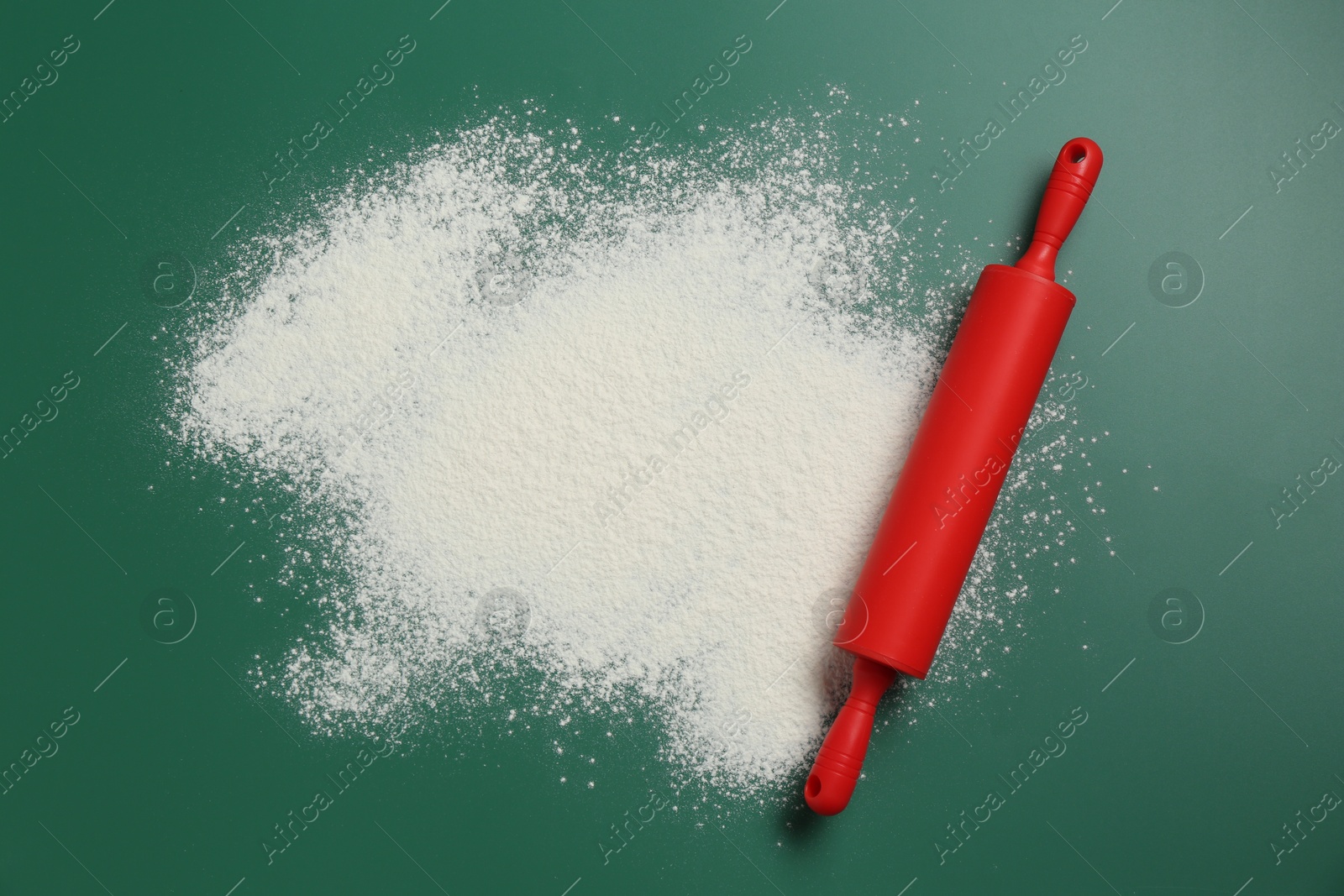 Photo of Red rolling pin and flour on green background, top view. Space for text