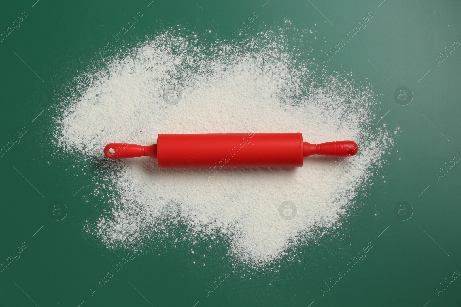 Photo of Red rolling pin and flour on green background, top view